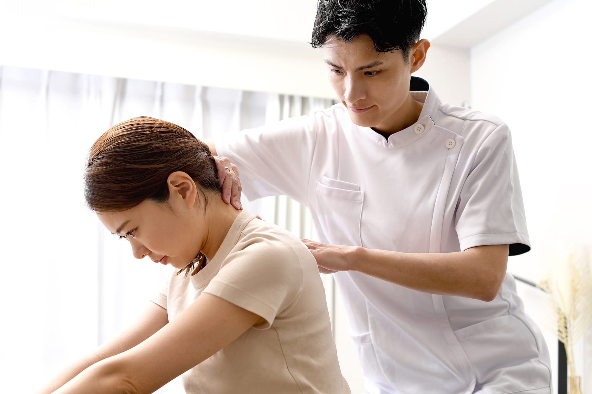 男性柔道整復師が女性の首を施術している風景。